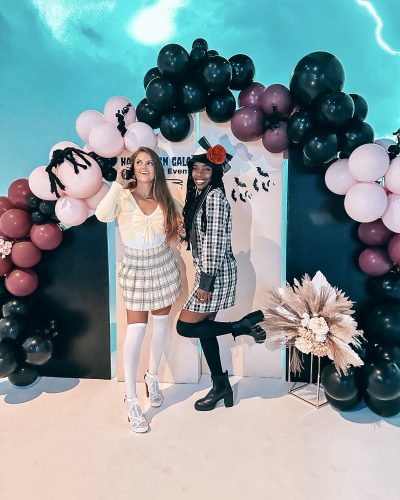 Two girls posing in front of a Halloween themed back drop in their Halloween costumes